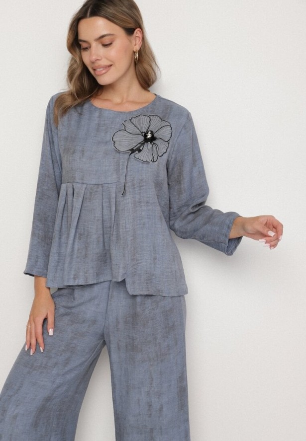 Niebieski Komplet Bluzka z Rozkloszowanym Dołem i Aplikacją Kwiatka i Luźne Spodnie Ravirisa